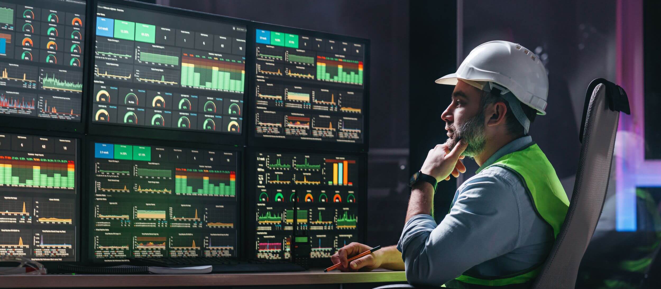 A man looking at four screens with multiple charts and graphs on it.