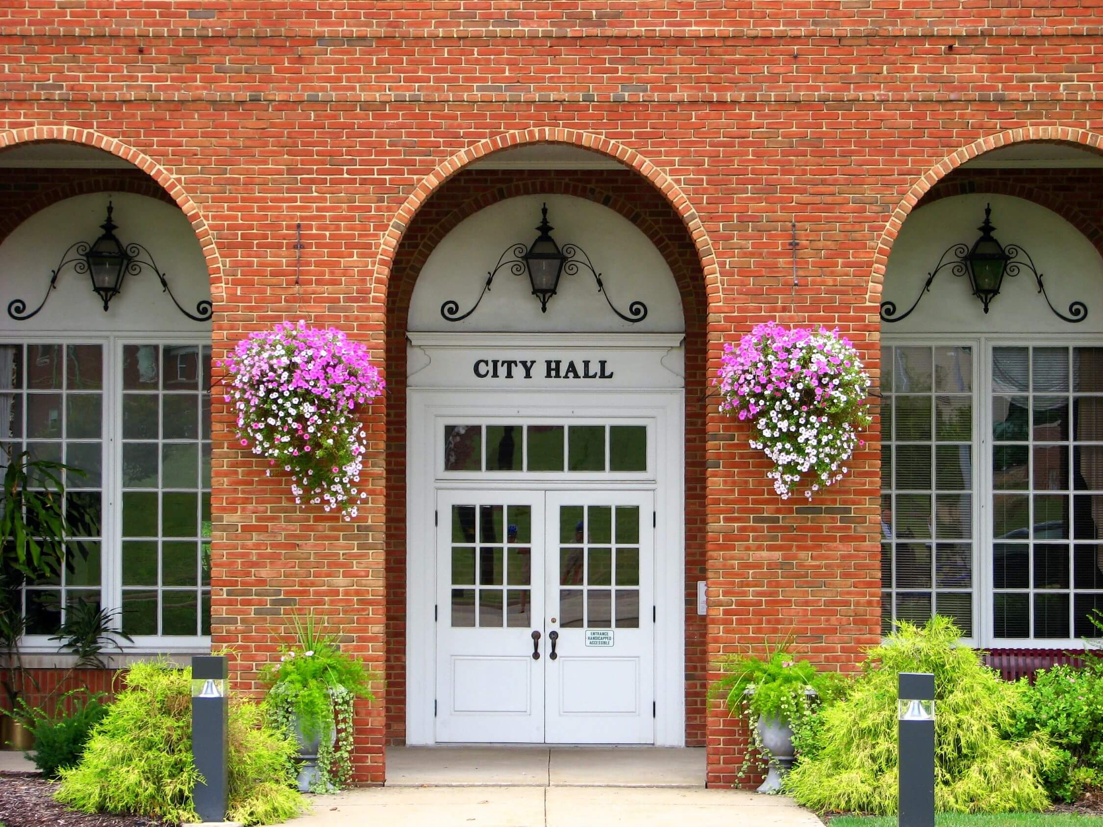 A traditional brick City Hall building with arched windows, decorative flower arrangements, and a welcoming entrance.