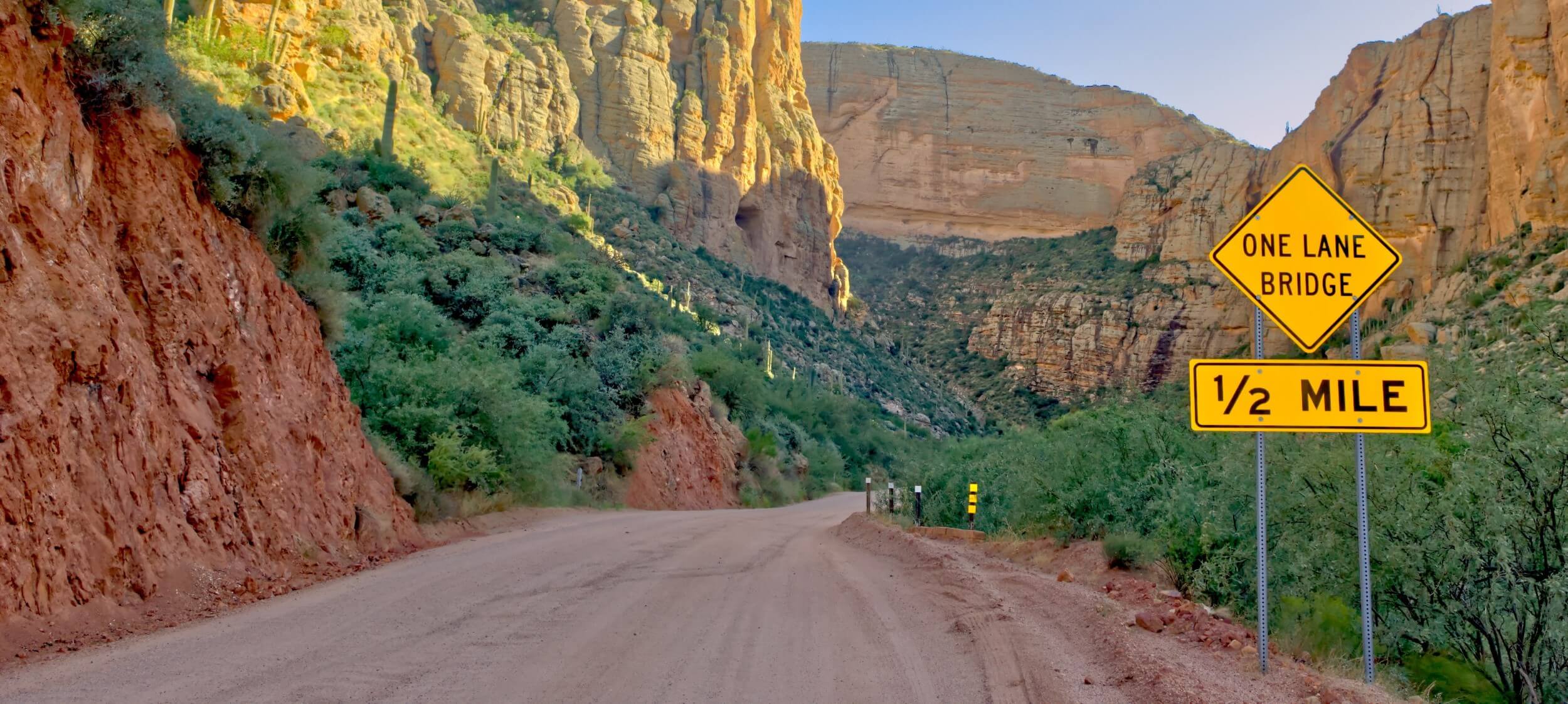 Dirt section of Arizona State Route 88 winding through rocky desert terrain, with a warning sign indicating a narrow road ahead. Dirt section of Arizona State Route 88 winding through rocky desert terrain, with a warning sign indicating a narrow road ahead.