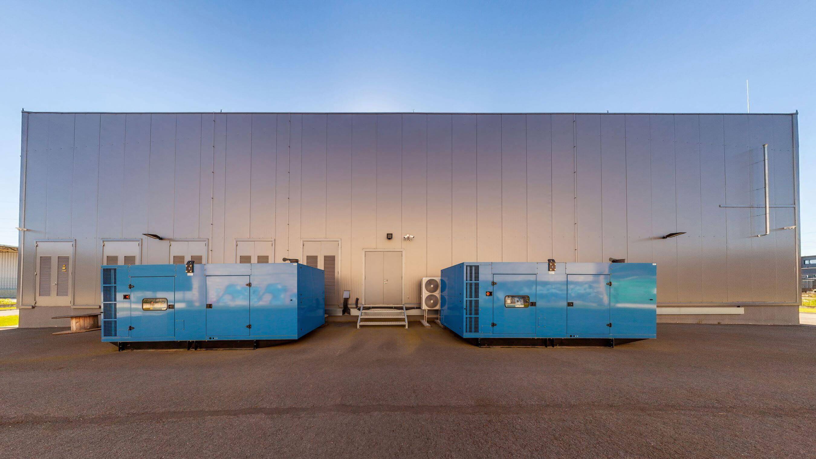 Exterior view of an industrial facility with two large blue backup generators, representing a modern data center infrastructure